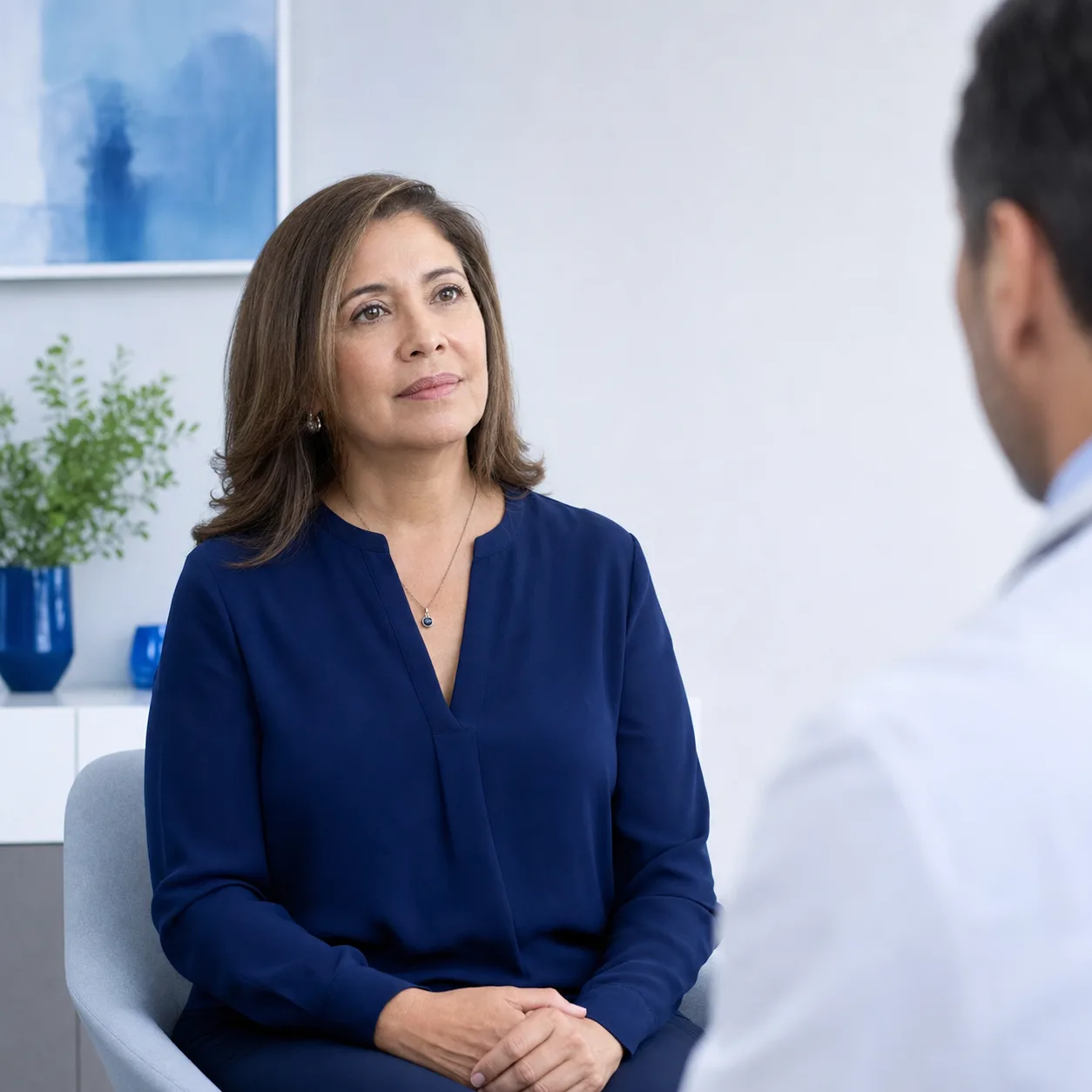 Paciente conversando con su médica en la consulta, de espaldas la profesional de bata blanca